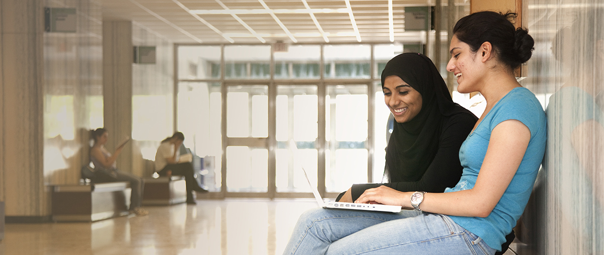 Two students sitting in hallway and looking at laptop screen