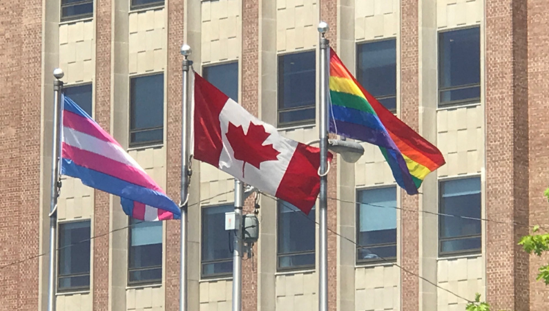 Pride flags flying along with the Canadian flag.