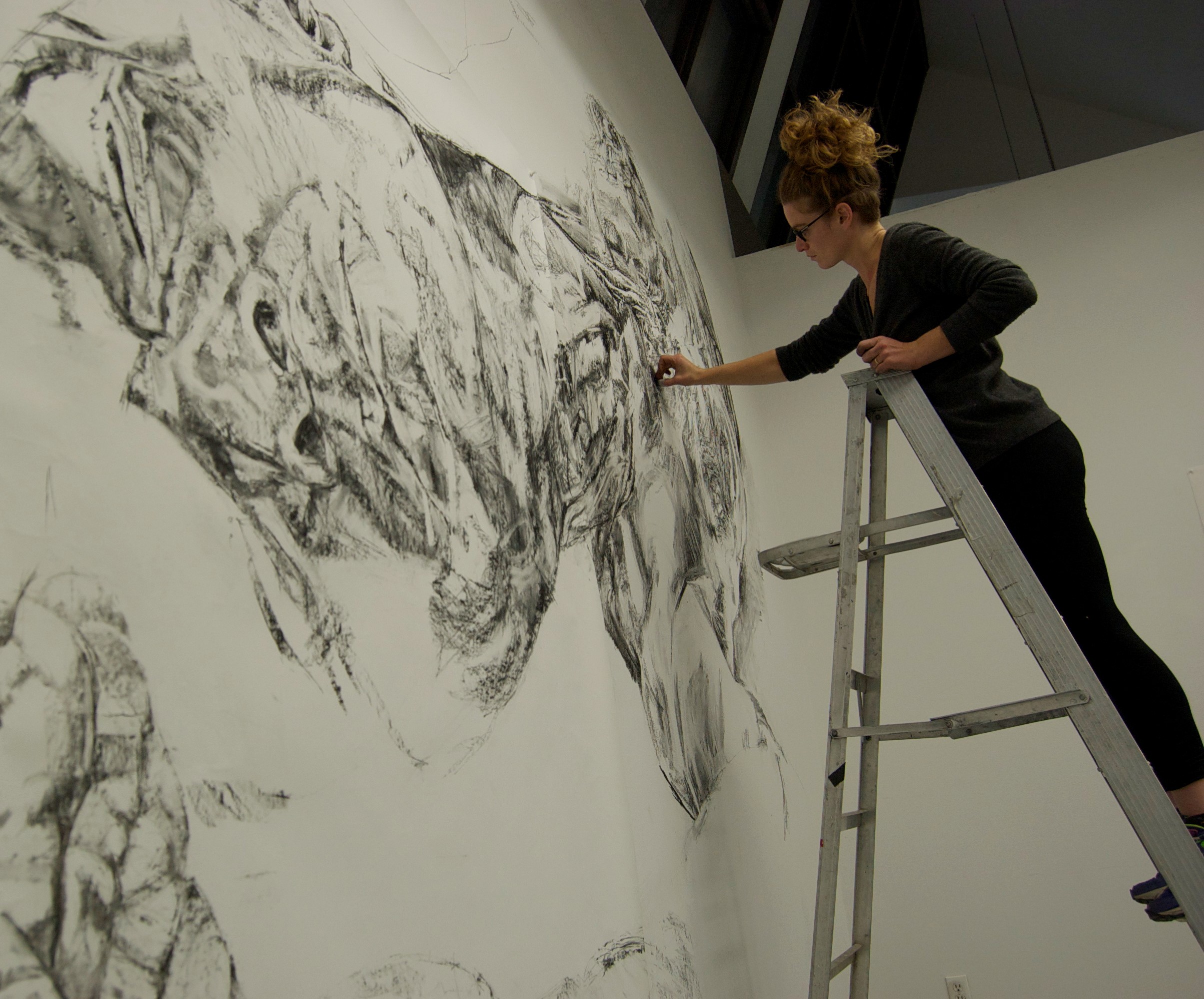 Esther McAdam standing on a ladder, drawing on a wall